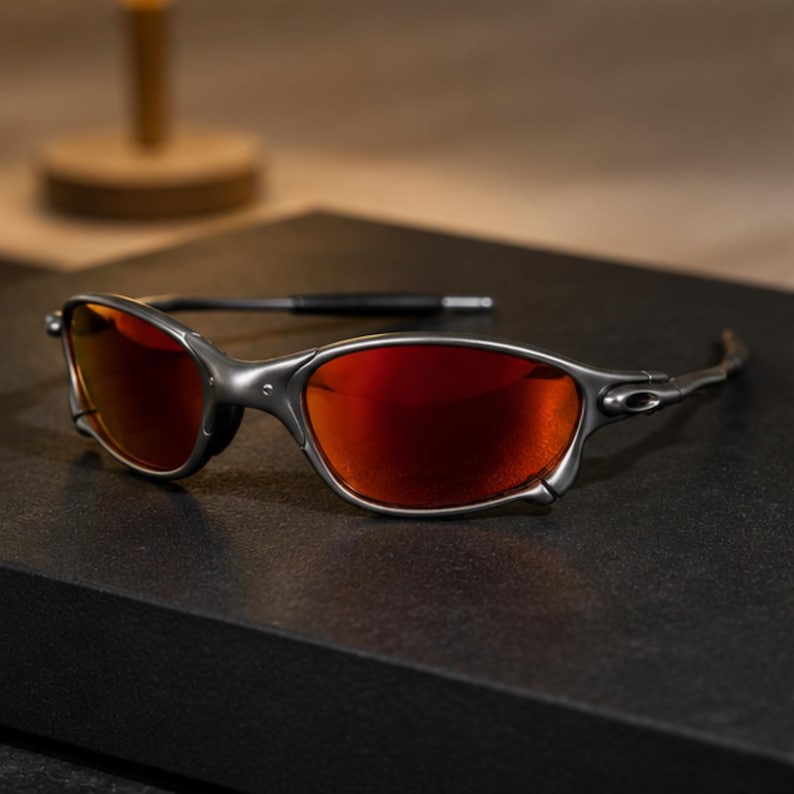 Peut inclure: Lunettes de soleil avec une monture gris m&eacute;tallique et des verres r&eacute;fl&eacute;chissants orange-rouge. Les lunettes pr&eacute;sentent un design enveloppant avec des branches fines et profil&eacute;es et des manchons noirs, affichant une esth&eacute;tique industrielle.
