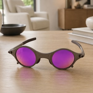 Puede incluir: Gafas de sol ovaladas con montura marrón y lentes moradas. Las gafas de sol tienen un diseño único con un puente y patillas curvados. Las lentes reflejan un tono púrpura vibrante.
