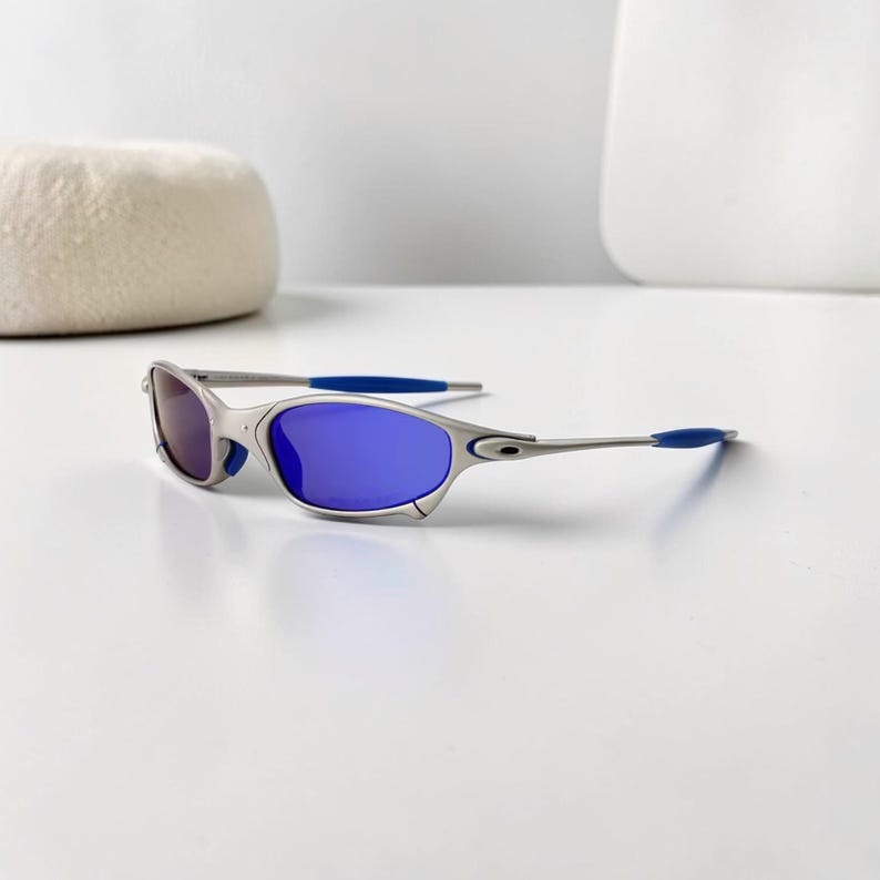 May include: Silver-framed sunglasses with blue lenses and blue temple tips. The sunglasses have a sleek, modern design. The lenses are a vibrant blue color, and the frame is a metallic silver.