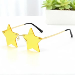 以下が含まれることがあります： 金色のフレームと黒いテンプルが付いた、黄色の星型のサングラス。 レンズは明るい黄色で、フレームは繊細でミニマリストなデザインです。 楽しくて人目を引くアクセサリーです。