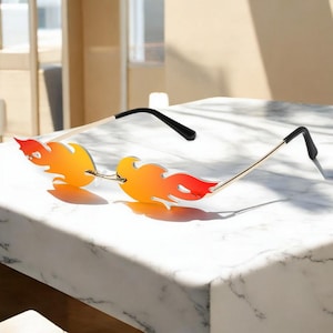May include: A pair of flame-shaped sunglasses with a gold frame and orange and yellow gradient lenses.