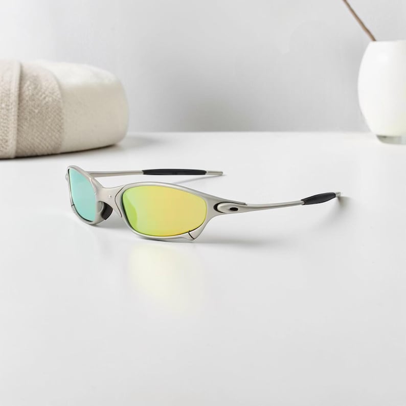 May include: Silver-framed sunglasses with yellow and green mirrored lenses. The sunglasses have a sleek, modern design with black temple tips. The lenses reflect a gradient of colors, adding a stylish touch to the eyewear.