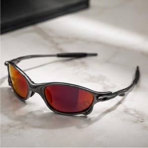 Peut inclure: Lunettes de soleil avec une monture gris m&eacute;tallique fonc&eacute; et des verres r&eacute;fl&eacute;chissants rouge orang&eacute;. Les lunettes pr&eacute;sentent un design enveloppant avec des branches fines et incurv&eacute;es et des embouts en caoutchouc noir pour un usage ext&eacute;rieur.