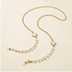 Peut inclure: Une chaîne de lunettes en métal doré ornée de petites perles blanches artificielles et de deux breloques blanches en forme de trèfle à quatre feuilles. La chaîne comporte des boucles en silicone transparent aux extrémités pour les lunettes.