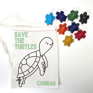 May include: A white canvas bag with a drawstring closure. The bag has a green outline of a turtle and the text "SAVE THE TURTLES" in green. The bag also has the word "CONRAD" printed on it. The bag is filled with colorful turtle-shaped crayons.