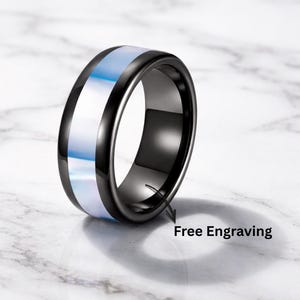 May include: A black ring with a central band of iridescent white and blue. The ring has a polished finish and the text "Free Engraving" is visible.