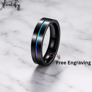 Puede incluir: Un anillo negro con una fina franja iridiscente azul y morada. El anillo está sobre un fondo de mármol. El texto "Free Engraving" es visible.