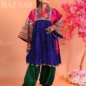 Puede incluir: Un vibrante vestido afgano tradicional con corpi&ntilde;o rosa, falda azul y pantal&oacute;n verde. El vestido presenta intrincados bordados y adornos. La imagen incluye el texto "KOCHAI BAZAAR".