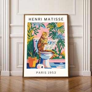 May include: A framed art print featuring a cat reading a newspaper while sitting on a toilet. The artwork has a colorful, Matisse-inspired style with the text "HENRI MATISSE PARIS 1953". The background includes plants and a pink wall.