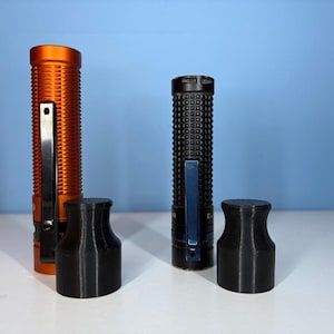 May include: Two flashlights, one orange and one black, with black pocket clips, and two black cylindrical caps. The orange flashlight has a ribbed texture. The black flashlight has a textured, grid-like pattern. The caps are cylindrical with a flared top.