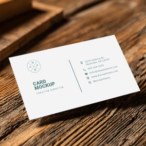 May include: A white business card mockup with the text "CARD MOCKUP" and "CREATIVE DIRECTOR" in a sans-serif font. The card includes contact information and a circular logo. The card rests on a textured wooden surface.