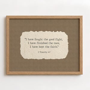 May include: A framed wall art piece featuring a light brown grid pattern background and a central piece of cream-coloured paper with torn edges. The text reads: "I have fought the good fight, I have finished the race, I have kept the faith." 2 Timothy 4:7.