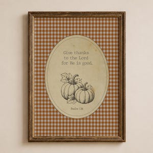 May include: A framed wall art print featuring a brown and white gingham background. In the center, an oval contains the text 'Give thanks to the Lord for He is good.' and 'Psalm 136' above a black and white line drawing of two pumpkins.