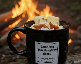 May include: A black speckled mug candle with the text "Campfire Marshmallow Cocoa" on a white label. The candle is filled with white wax, marshmallow-shaped wax pieces, and caramel-colored wax pieces. A campfire burns in the background.