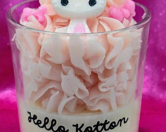 May include: A clear glass candle with a pink and white design. The candle features a Hello Kitty figurine and is surrounded by a swirl of pink wax. The text "Hello Kotton Kandy" is printed on the front.