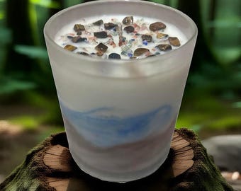 May include: A frosted glass candle with a white wax interior and colorful stones on top. The candle has a blue and brown painted design on the exterior. The candle is sitting on a tree stump.