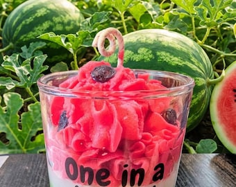 May include: A watermelon-themed candle in a clear glass, with red, white, and green layers. The candle is topped with red wax and dark accents. Text on the glass reads "One in a Melon!". The candle is 10 oz / 283 g. Watermelons and foliage are in the background.