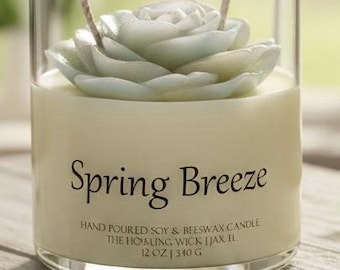 May include: A glass candle holder with a light green, rose-shaped wax top. The candle is labeled "Spring Breeze" and contains 12 oz of wax. The candle is made with soy and beeswax.