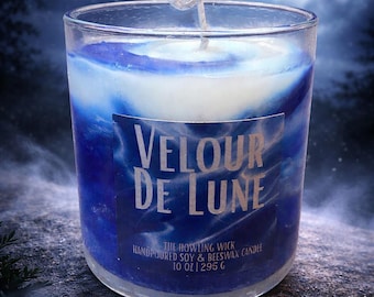 May include: A glass candle with blue and white wax, labeled "VELOUR DE LUNE." The candle is 10 oz (295 g) and has a wick. The background features a full moon and a cloudy night sky.