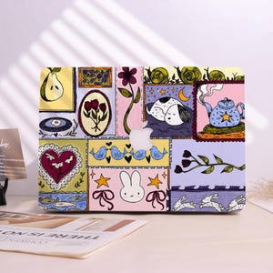 Könnte beinhalten: Eine farbenfrohe Laptop-Hülle mit einem Patchwork-Design mit skurrilen Illustrationen. Das Design umfasst eine Birne, Tulpen, Vögel, einen schlafenden Hund, eine Teekanne, ein Herz, ein Kaninchen und Schnecken.