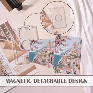 May include: Transparent phone case with a magnetic detachable design. The case displays a coastal town illustration with pink buildings, flowers, and a scooter. The text "MAGNETIC DETACHABLE DESIGN" is at the bottom.