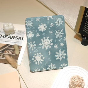 Könnte beinhalten: Eine blaue Tablet-Hülle mit einem Muster aus weißen Schneeflocken. Die Hülle hat eine rechteckige Form und eine matte Oberfläche. Die Schneeflocken variieren in Größe und Design und erzeugen ein winterliches Thema.