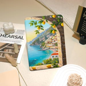 Peut inclure: Une coque de tablette rectangulaire avec une peinture d'une ville côtière italienne. L'œuvre est encadrée par une arche en pierre avec des branches de citron. La scène comprend une mer bleue, des bâtiments colorés et un ciel lumineux.