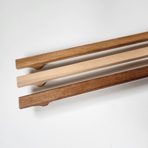 May include: Three wooden cabinet pulls in varying shades of brown. The top pull is a light brown, the middle is a natural wood tone, and the bottom is a dark brown. Each pull has a curved handle.