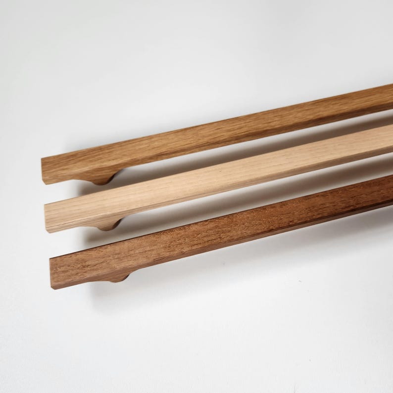 May include: Three wooden cabinet pulls in varying shades of brown. The top pull is a light brown, the middle is a natural wood tone, and the bottom is a dark brown. Each pull has a curved handle.