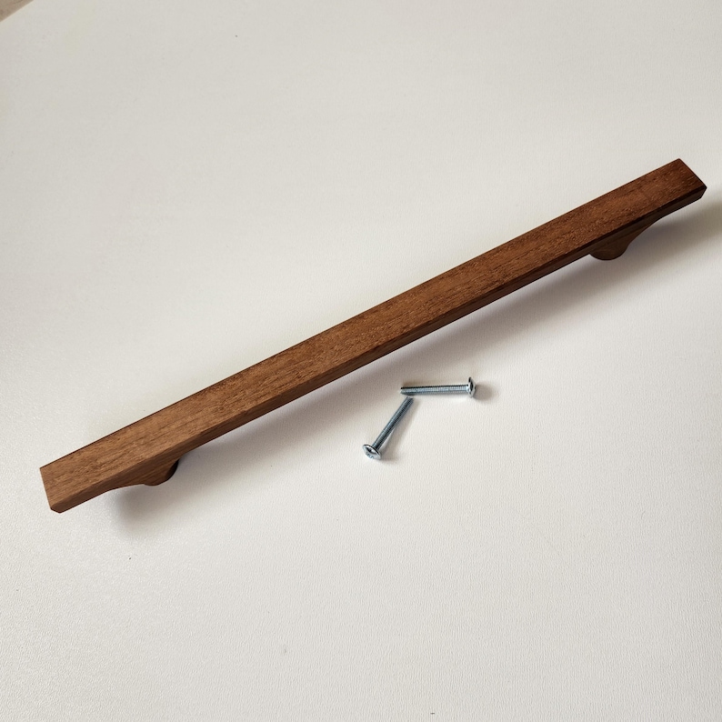 May include: A rectangular wooden cabinet pull with a rich brown finish. Two silver screws are included. The pull measures approximately 12 inches in length.