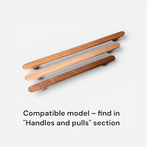 May include: Three wooden cabinet pulls in varying shades of brown, from light to dark. The pulls are rectangular with rounded ends and are arranged diagonally against a white background. Text at the bottom reads "Compatible model - find in "Handles and pulls" section."