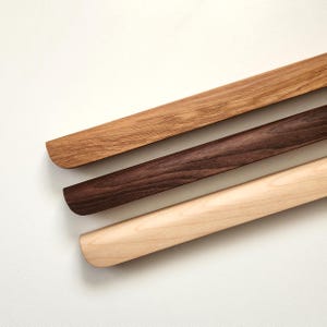 以下が含まれることがあります： さまざまな茶色の木製ハンガーが3つ。一番上のハンガーは明るい茶色、真ん中は濃い茶色、一番下は明るいベージュ色です。各ハンガーは丸みを帯びた端を持っています。