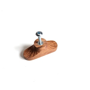 May include: A wooden cabinet knob with a silver screw. The knob is a light brown color and has a unique, curved shape. The wood grain is visible, adding texture. This hardware is suitable for drawers and cabinets.
