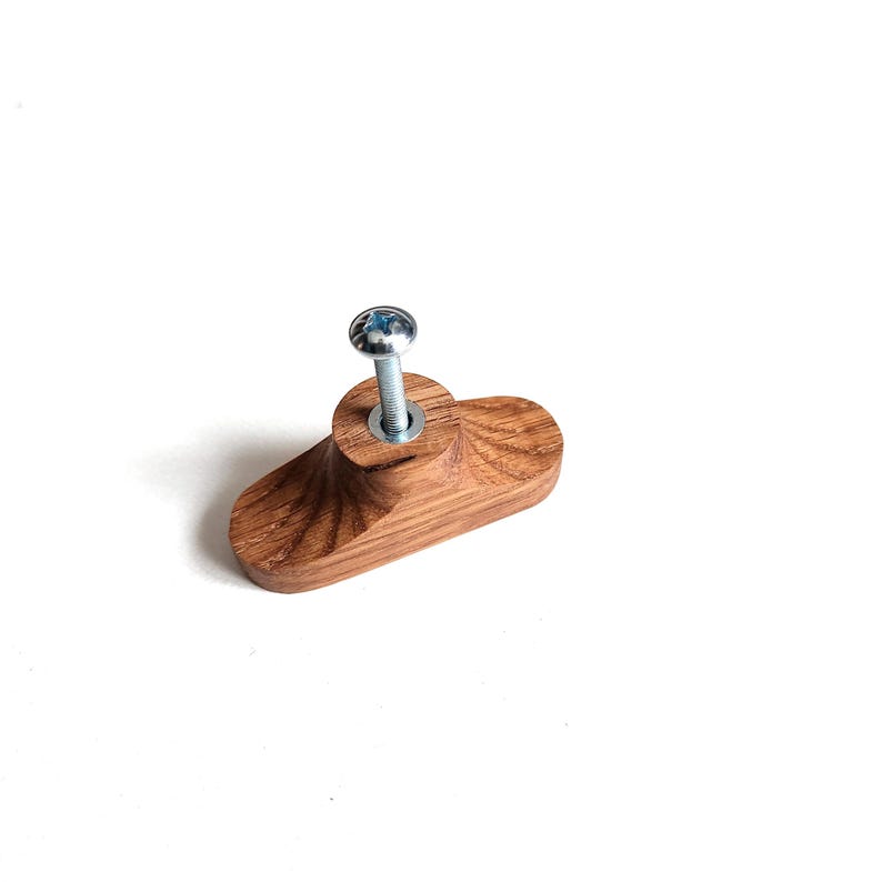 May include: A wooden cabinet knob with a silver screw. The knob is a light brown color and has a unique, curved shape. The wood grain is visible, adding texture. This hardware is suitable for drawers and cabinets.