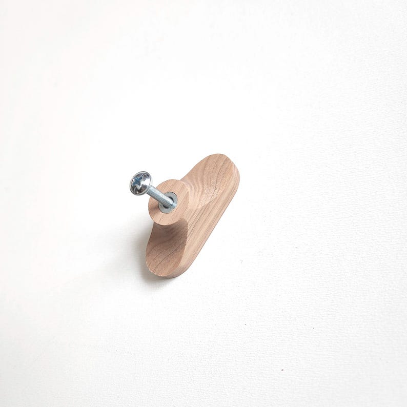 May include: A light-colored wooden cabinet knob with a silver screw. The knob is oval-shaped and has a natural wood grain. The screw is attached to the center of the knob.