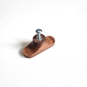May include: A wooden cabinet knob with a dark brown finish. The knob has a rounded, oblong shape with a cylindrical base. A silver screw is inserted through the center for attachment. The knob is designed for furniture and cabinetry.
