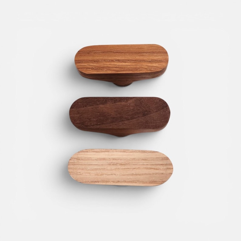 May include: Three wooden cabinet knobs in varying shades of brown. The top knob is a light brown, the middle is a dark brown, and the bottom is a light tan. Each knob has a rounded rectangular shape with a small, curved handle.