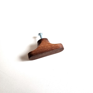 May include: A wooden cabinet knob with a dark brown finish and a silver screw. The knob has a T-shape design and is set against a white background. This hardware is suitable for drawers and cabinets.