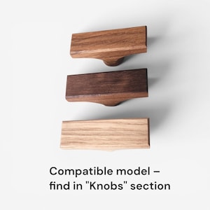 May include: Three wooden cabinet knobs in varying shades of brown, arranged vertically against a white background. The knobs have a rectangular top and a rounded base. Text at the bottom reads "Compatible model - find in "Knobs" section."