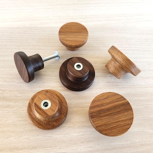 Könnte beinhalten: Eine Auswahl an Holzschrankknöpfen in verschiedenen Formen und Ausführungen. Die Knöpfe umfassen runde, herzförmige und abgestufte Designs mit hellen und dunklen Brauntönen. Einige Knöpfe haben sichtbare Schrauben.