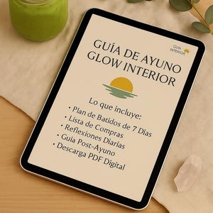 May include: A digital tablet displays the text "GUÍA DE AYUNO GLOW INTERIOR" with a sun graphic. The tablet is on a wooden surface, next to a green smoothie in a glass jar and a sprig of leaves.