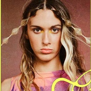 May include: A woman with long blonde hair and a pink and purple tie-dye shirt. She is wearing a pearl necklace. The image is set against a yellow background with the text "Services:" and a list of services: "Women's Haircut" and "Blow Dry".