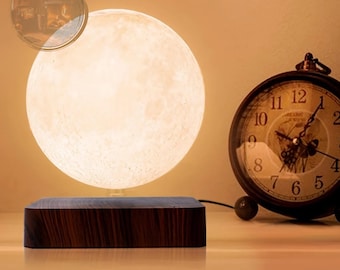 May include: A white moon-shaped lamp with a wood base, levitating above the base. The lamp is lit and casting a warm glow. A vintage clock is in the background.