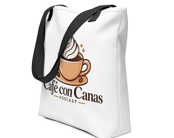 May include: A white tote bag with black shoulder straps featuring a graphic of a tan coffee cup with whipped cream and two coffee beans. Below the cup, the text reads Café con Canas PODCAST in dark brown letters with two horizontal lines.
