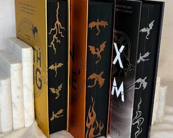 Peut inclure: Trois livres à couverture rigide debout avec des dos métalliques dorés, cuivrés et argentés. Les tranches noires présentent des motifs en feuille d'or, de cuivre et d'argent représentant des dragons, des éclairs et des flammes. Les dos affichent le texte HARRY POTTER AND THE GOBLET OF FIRE et XM.