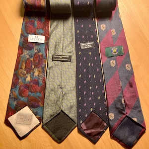 Puede incluir: Cuatro corbatas de seda con varios diseños y colores. Una corbata presenta un diseño floral, otra un patrón geométrico, una tercera un patrón de diamantes y la última rayas diagonales. Cada corbata tiene una etiqueta de marca.