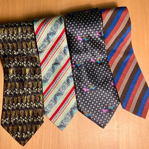 Puede incluir: Se muestran cinco corbatas estampadas con diversos diseños y colores. Las corbatas presentan diseños florales, a rayas y de lunares. Los colores incluyen negro, rojo, azul, marrón y verde.