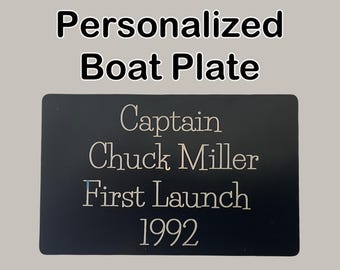 Könnte beinhalten: Schwarzes Bootsnamensschild mit dem Text "Captain Chuck Miller First Launch 1992" in silbernen Buchstaben.