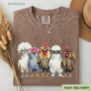 May include: A brown t-shirt with a graphic print of five chickens wearing various styles of sunglasses. The shirt features a crew neckline and a label reading Comfort Colors. The chickens are depicted in white, grey, brown, and black colors.