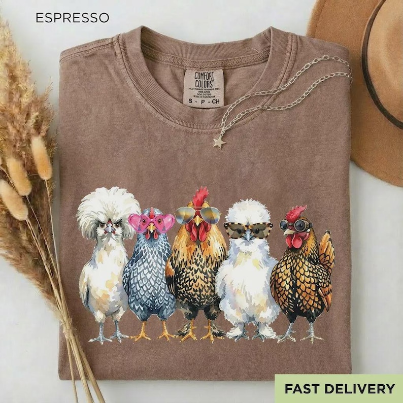 May include: A brown t-shirt with a graphic print of five chickens wearing various styles of sunglasses. The shirt features a crew neckline and a label reading Comfort Colors. The chickens are depicted in white, grey, brown, and black colors.